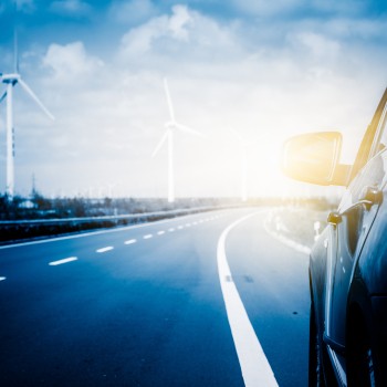 Wind turbines on landscape along empty road against sky.
